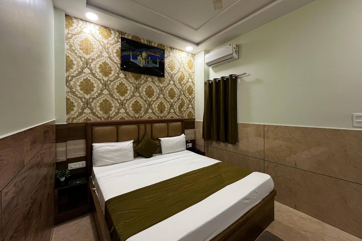 Une chambre d’hôtel comprenant un lit, une table de chevet, un appareil de climatisation, un téléviseur fixé au mur et un papier peint à motifs.