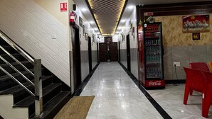 Un couloir avec un sol carrelé, un escalier sur la gauche, un distributeur automatique sur la droite et un extincteur accroché au mur.