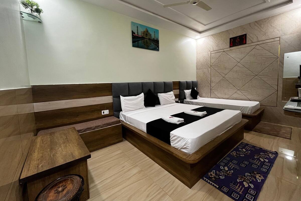 Une chambre d’hôtel avec deux lits, une tête de lit en bois, une table de chevet, une petite table, un miroir et un ventilateur de plafond.
