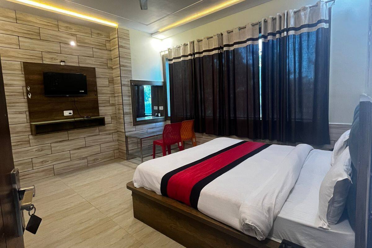 Une chambre d’hôtel moderne dotée d’un grand lit, d’un téléviseur à écran plat fixé à un mur en bois, d’un ventilateur de plafond et d’une salle de bain avec douche et toilettes.