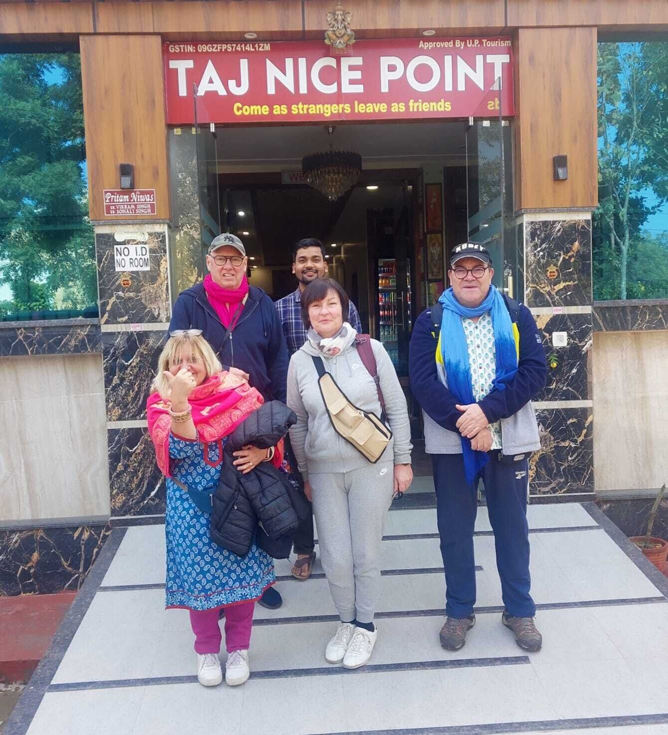 A group of people standing in front of Taj Nice Point, a building with a sign indicating it is approved by U.P. Tourism.