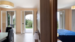 Een moderne kamer met een bed, een bureau en een stoel. Er zijn openslaande deuren naar een tuin.