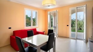 Een eetgedeelte met een glazen tafel, zwarte stoelen, een rode bank en een geel hanglamp.
