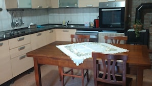 A kitchen with a dining table, chairs, cabinets, a stove, and a television.