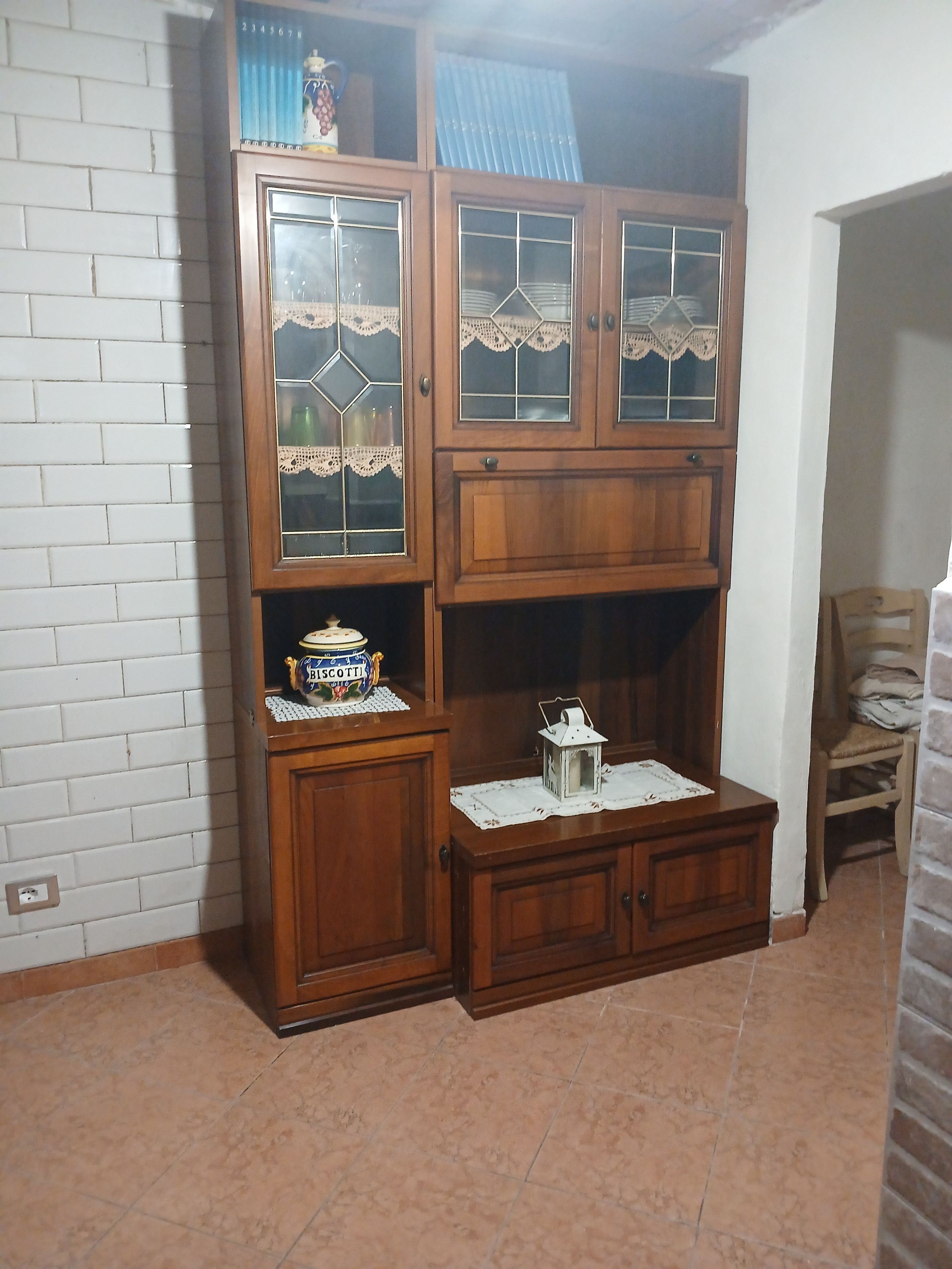 Un mobiletto in legno con ante in vetro e un piccolo ripiano con un barattolo.