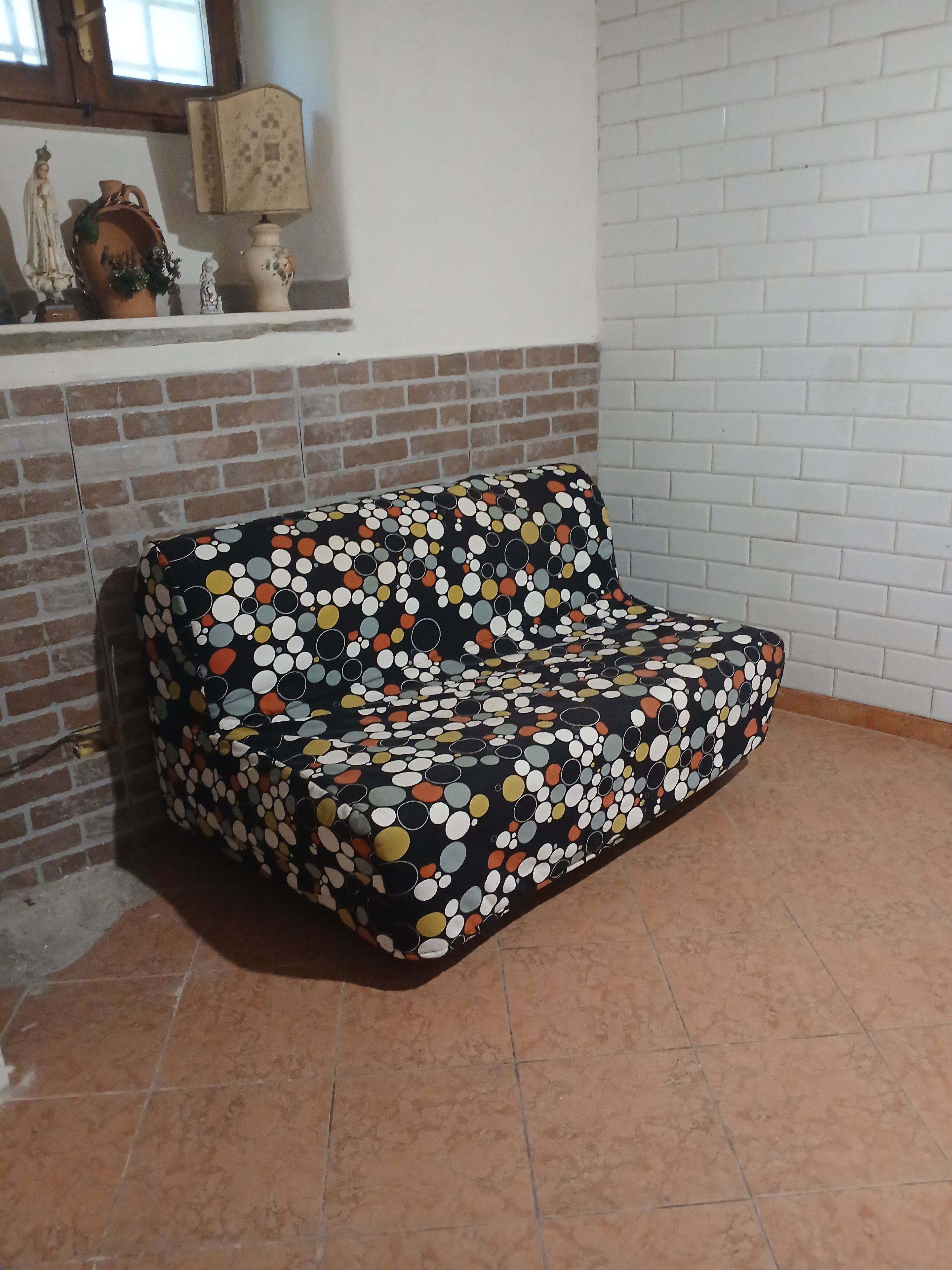 Ein Zimmer mit einer Couch an einer Ziegelwand, einem kleinen Regal mit Dekoration und einem gefliesten Boden.