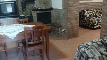 Ein gemütliches Wohnzimmer mit Kamin, einem Essbereich mit Tisch und Stühlen sowie einem gemusterten Sofa.