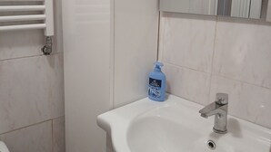 A bathroom with a white sink, a mirror, a towel rack, and a bottle of hand soap.
