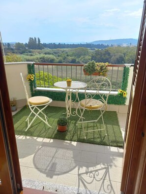Un balcon avec une table et des chaises, un pot de fleurs et une vue sur la campagne.