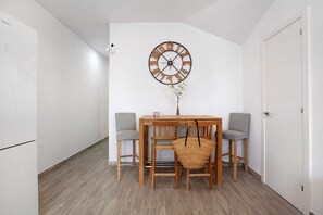 Un coin repas avec une table en bois, quatre chaises, une horloge murale et un petit vase avec des fleurs.