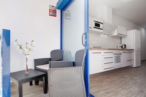 A modern kitchen with white cabinets, a microwave, and a coffee maker. There is a small dining area with two chairs and a table, and a vase with white flowers.