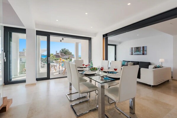 A modern interior with a dining area, white furniture, and large glass doors leading to an outdoor patio.
