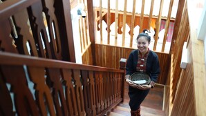 A wooden staircase with intricate railings and a person holding a tray.