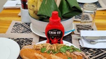 A dining table with a plate of food, a bowl of bananas, and a bottle of sauce.