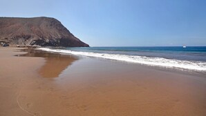 A beach with a rocky cliff and a sailboat in the distance. - Vacation Home "Estudio Sagrario" with Shared Pool (Arona)