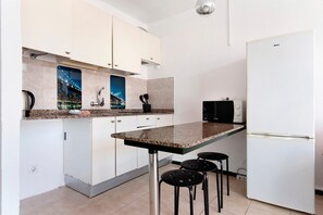 A kitchen with a granite countertop, white cabinets, a white refrigerator, and a black microwave.