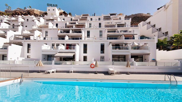 Uma piscina com uma boia salva-vidas, edifícios brancos e uma placa com a inscrição 'OMAR'.