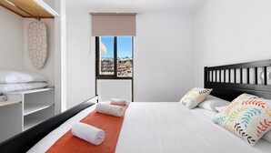 Quarto de hotel com cama, janela com vista, prateleira de madeira e decoração na parede.