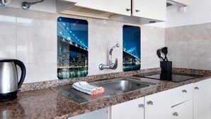 Cozinha moderna com pia de aço inoxidável, bancada de granito e vista para a cidade pela janela.