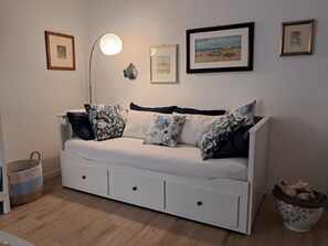 A white sofa with multiple pillows, a floor lamp, and framed pictures on the wall.