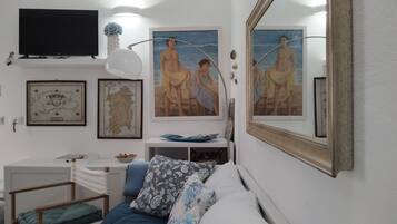 A room with a bed, a desk, a television, framed artwork, and a large mirror.
