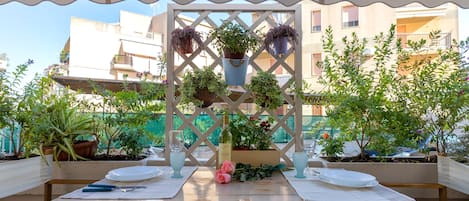 A table set outdoors with a white tablecloth, a wine bottle, and potted plants.