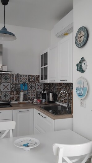 Een keuken met witte kasten, een spoelbak, een fornuis en een eethoek met een witte tafel en stoelen.