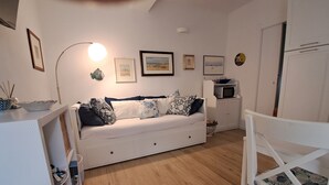 A white sofa with multiple pillows, a microwave, a white cabinet, and a white chair with a patterned cushion. - Apartment 'Casa Cordemar Alghero' with Private Terrace, Wi-Fi and Air Conditioning (Alghero)