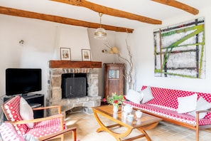 A living room with a stone fireplace, a television, a polka-dotted sofa, and a wooden ceiling beam.