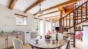A rustic kitchen with wooden beams, a dining table with chairs, a staircase, and a view of the outdoors. - Holiday Home 'Ville Daniel' with Private Terrace, Private Garden and Wi-Fi (PORDIC)