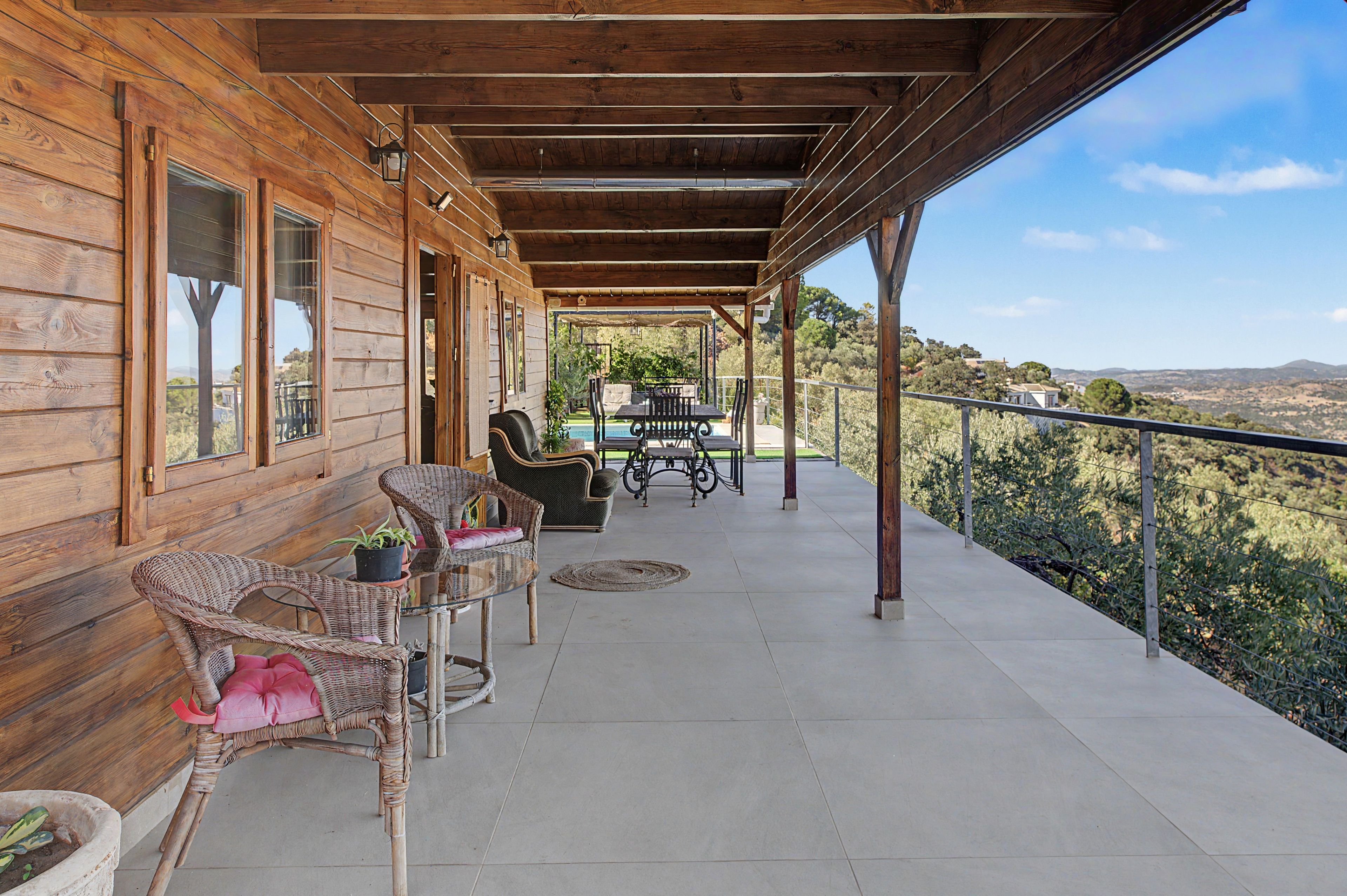 A wooden cabin with a covered porch, wicker furniture, and a view of the landscape.