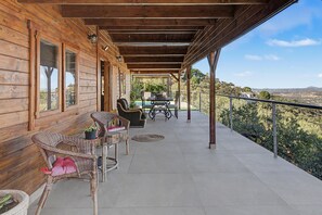 A wooden cabin with a covered porch, wicker furniture, and a view of the landscape. - Holiday Home 'Miralvalle' with Mountain View, Wi-Fi and Air Conditioning (El Gastor)