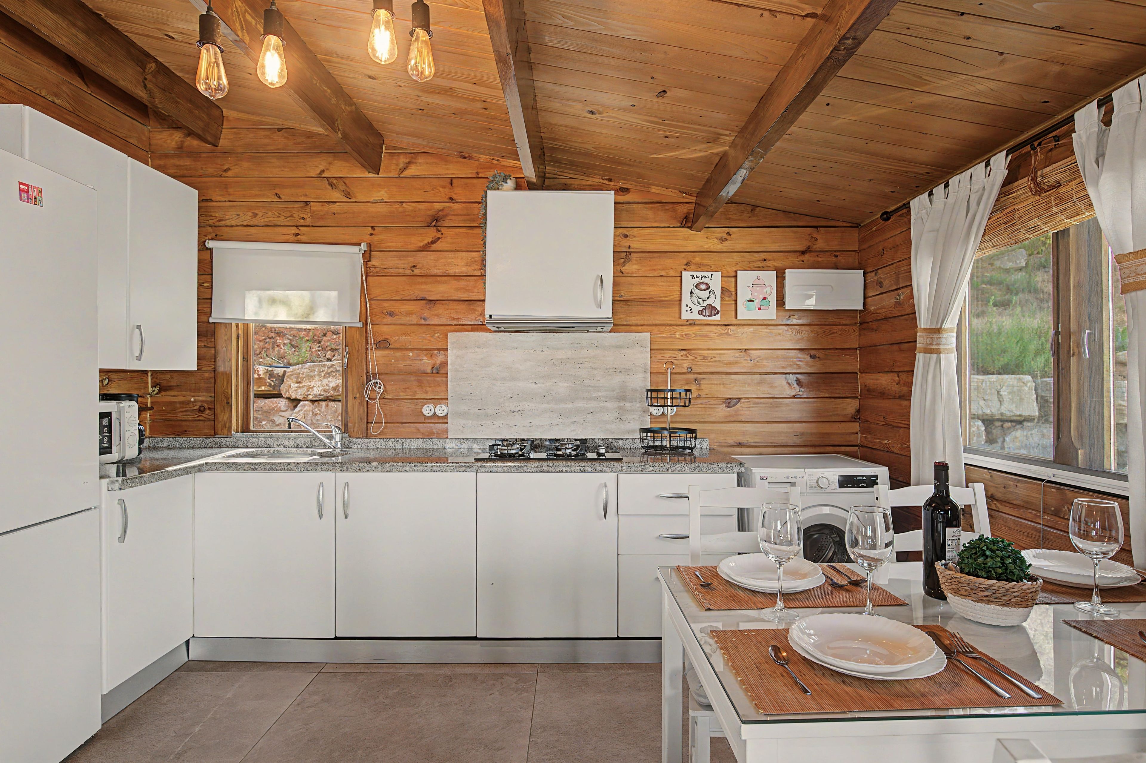 Une cuisine moderne avec des murs en bois, des armoires blanches, un comptoir en granit et un coin repas avec une table dressée pour deux personnes.