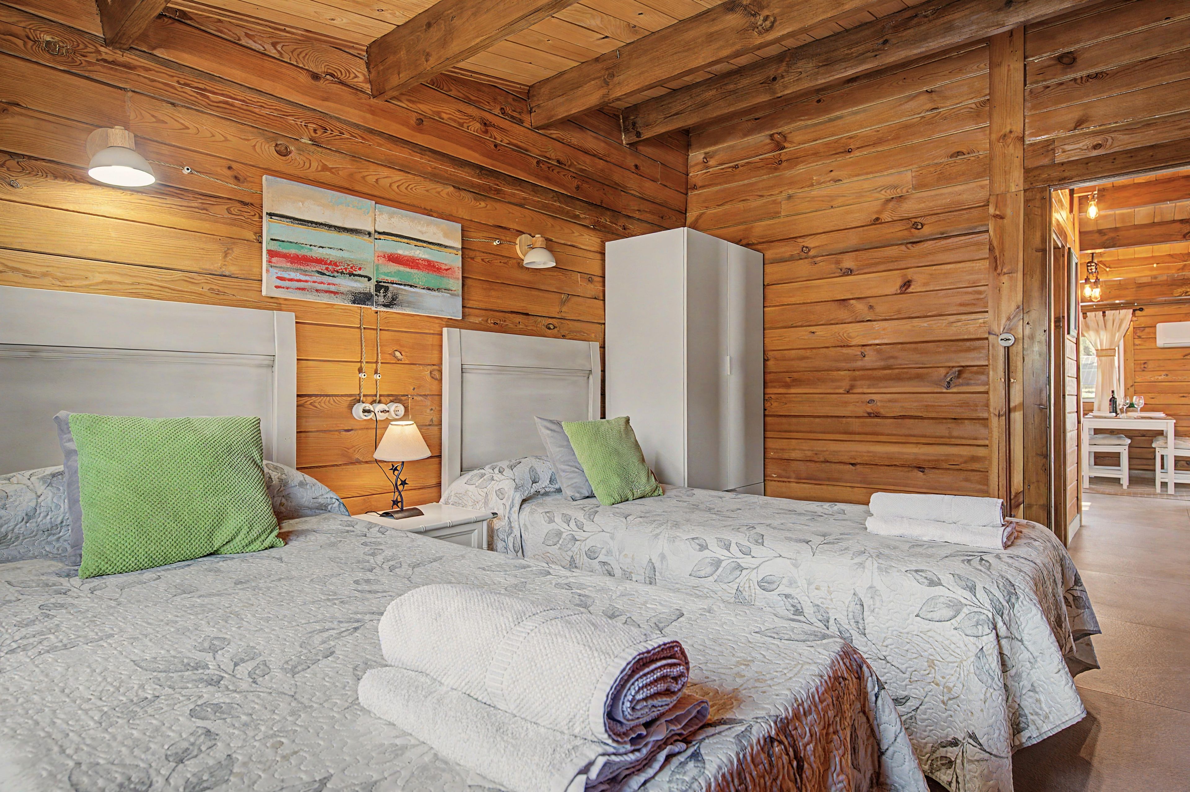 Ein Zimmer mit Holzwänden, zwei Betten, einem weißen Kleiderschrank und einem Gemälde an der Wand.