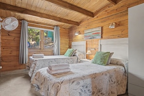 Habitación tipo cabaña de madera con dos camas, un ventilador y una ventana con cortinas.