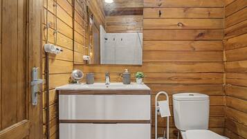 Une salle de bain aux murs lambrissés, équipée d’un lavabo, d’un miroir et de toilettes.