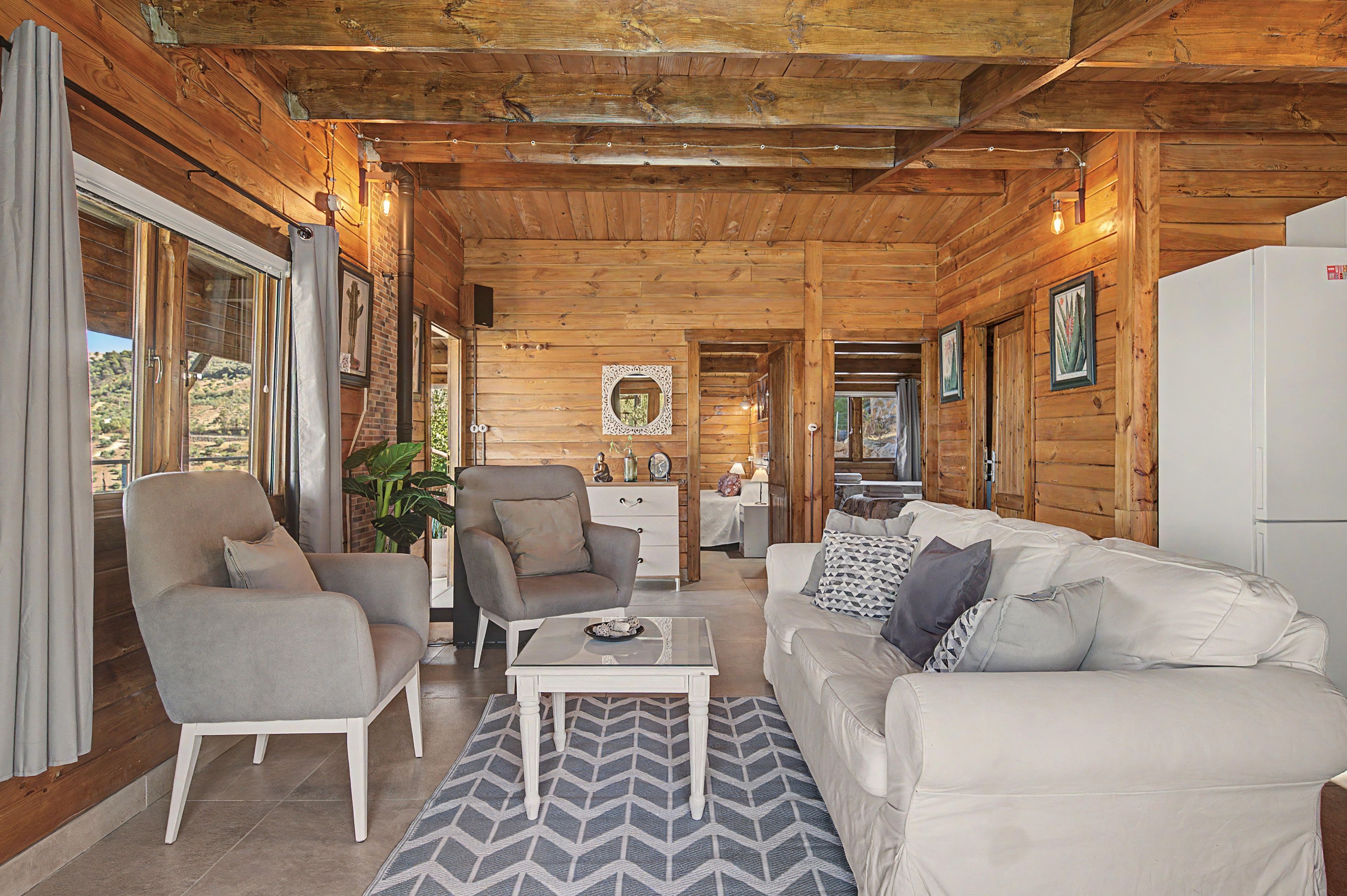 A cozy cabin interior with a wooden ceiling, a sofa, a chair, a coffee table, and a refrigerator.