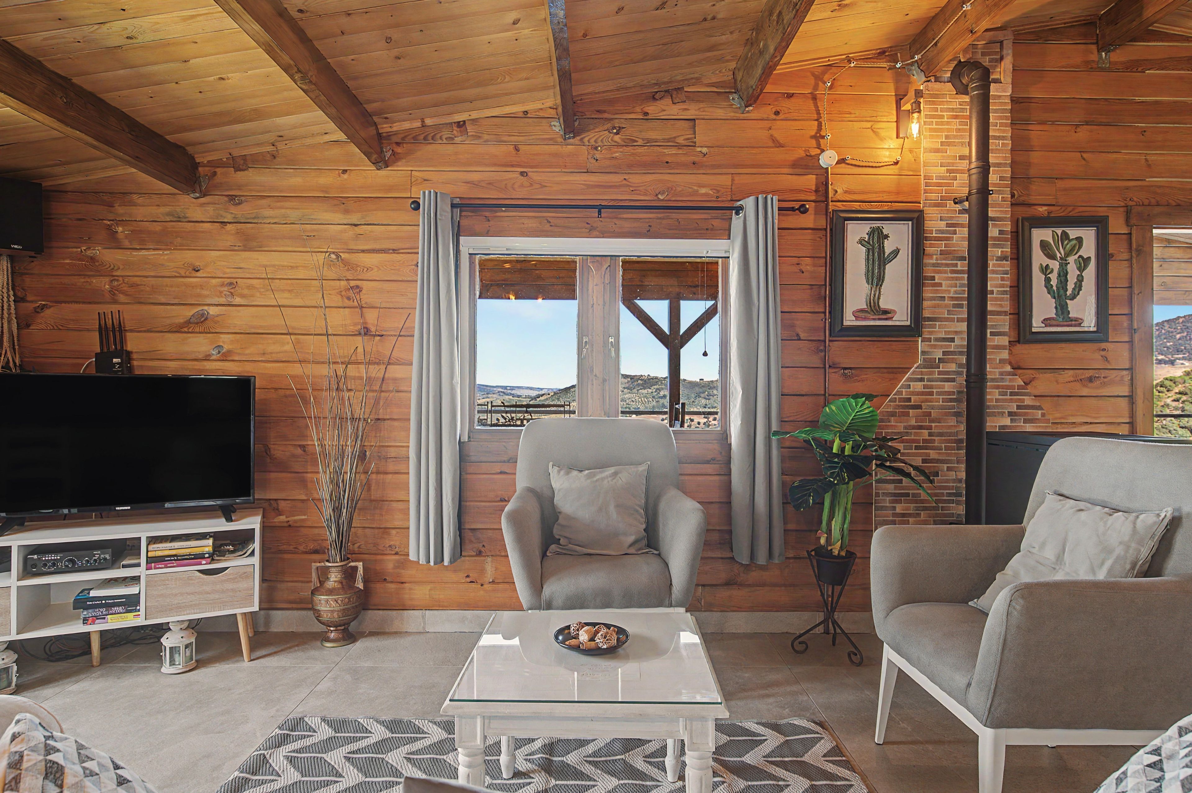 A cozy living room with a television, two armchairs, a coffee table, and a view through a window.