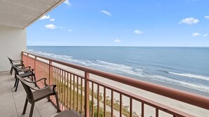 A balcony with a view of the ocean, featuring a railing and several chairs.