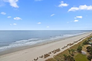 Una playa con una larga extensión de arena, un muelle a lo lejos y un cielo despejado.