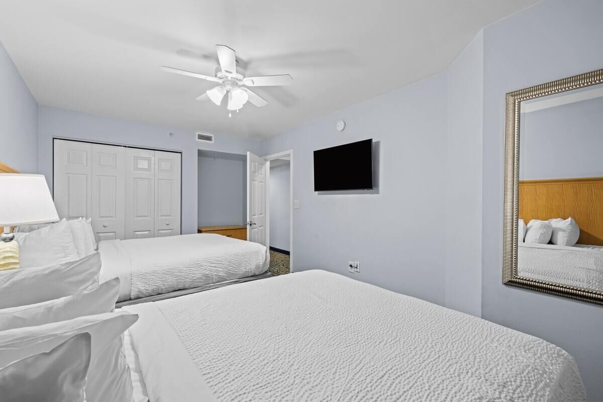 A hotel room with two beds, a ceiling fan, a TV, and a large mirror.