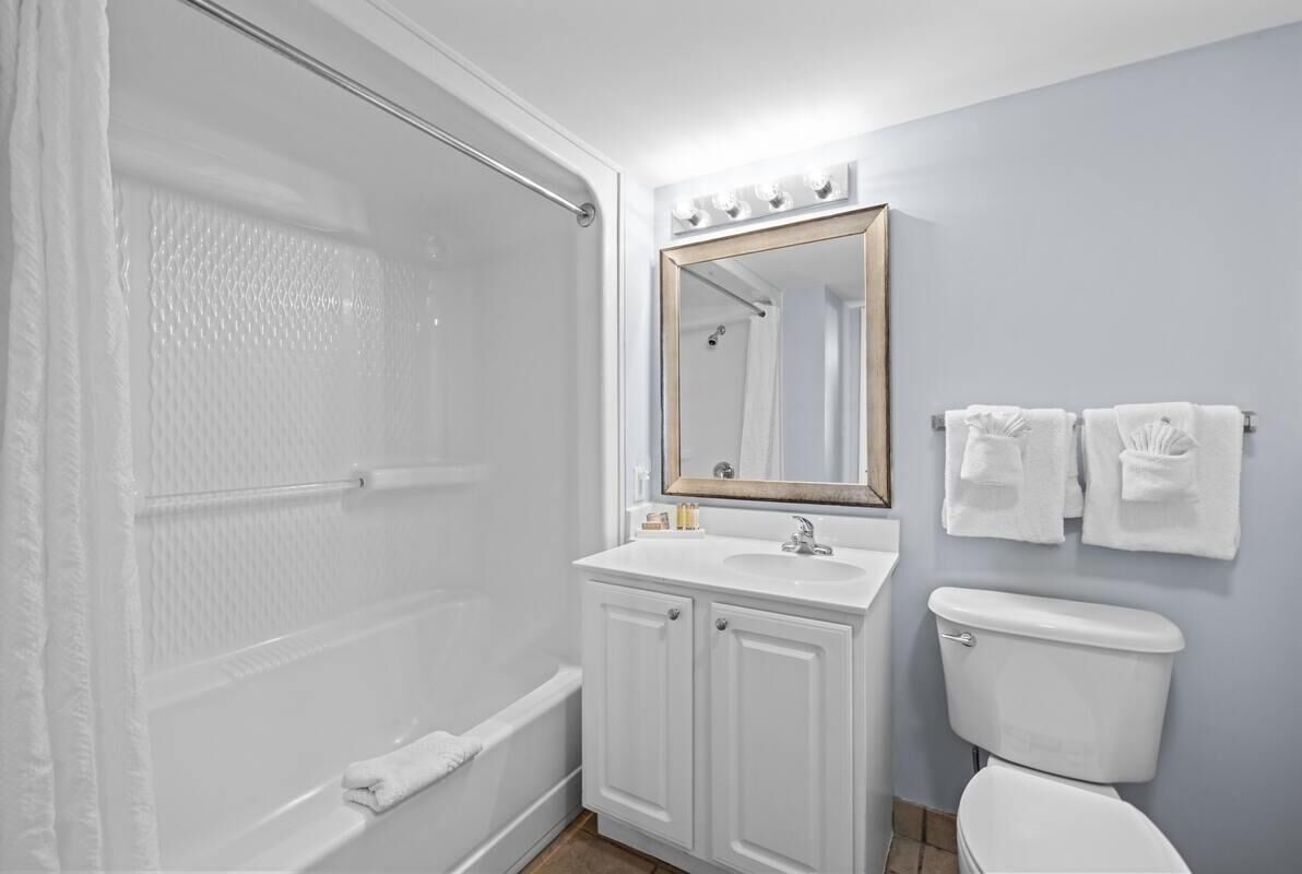 A bathroom with a shower, a sink with a mirror, and a toilet.