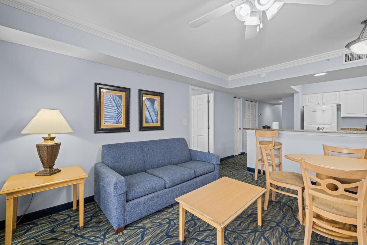 Ein Hotelzimmer mit einem blauen Sofa, einem Holztisch, einer Lampe und einer Küchenzeile.
