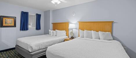 Habitación de hotel con dos camas, ventilador de techo, ventana con cortinas y un cuadro en la pared.