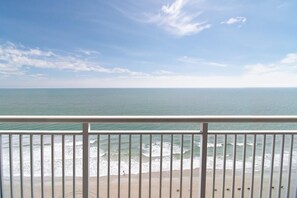 Blick auf einen Strand von einem Balkon mit Geländer, Meereswellen und einem klaren Himmel.