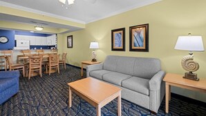 A hotel room with a sofa, a dining table, chairs, a small table with a lamp, a ceiling fan, and framed artwork on the wall. - Oceanfront 3 BR Condo Tons of Amenities 6th Flr (Myrtle Beach)