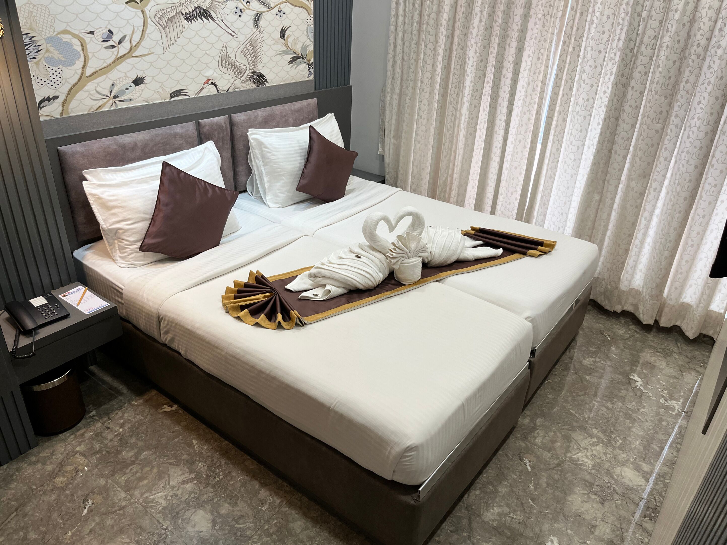 A neatly made bed with white linens, brown pillows, and a towel arrangement.