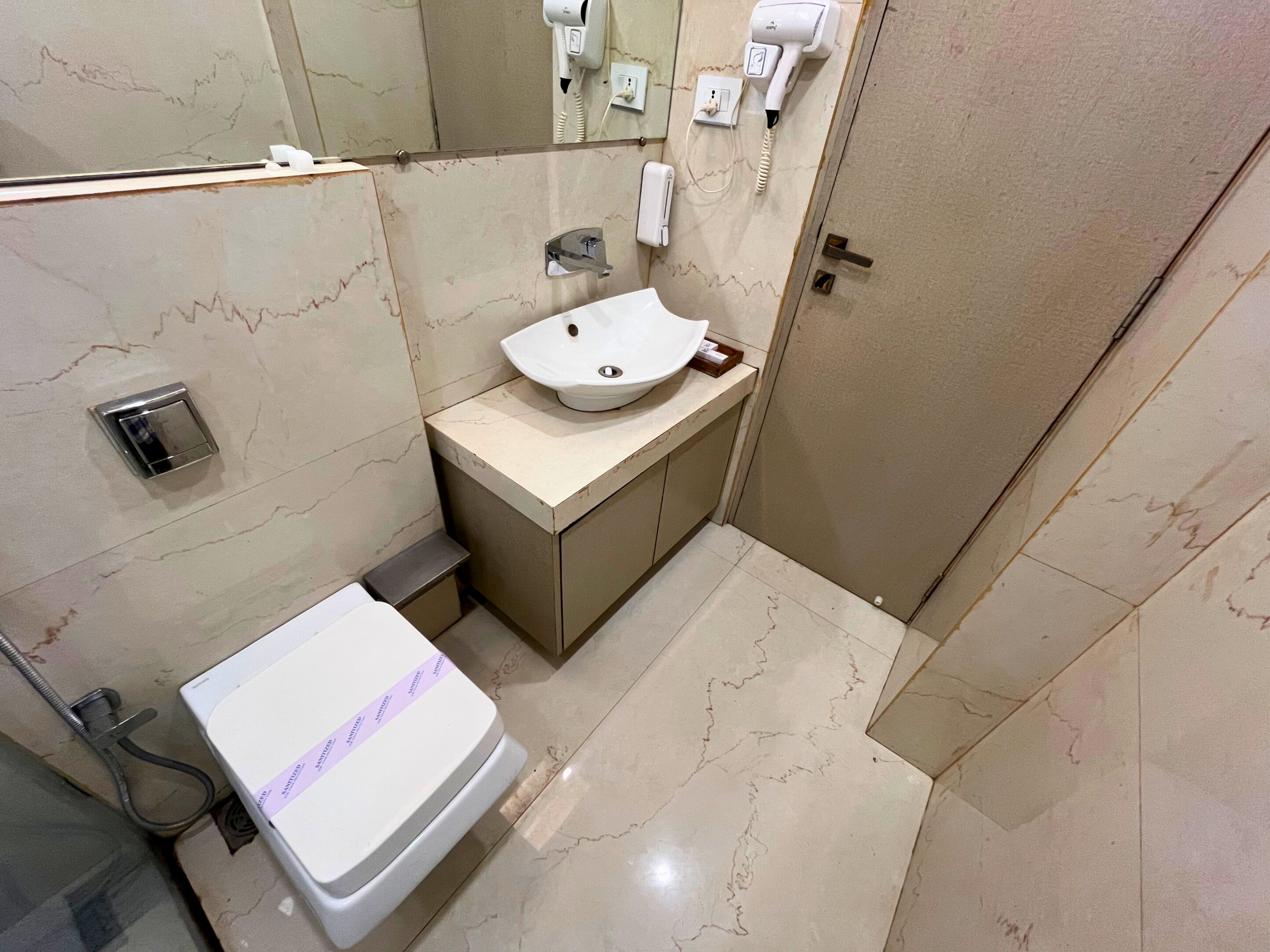 Een badkamer met een witte wastafel, een spiegel, een handdroger en een toilet.