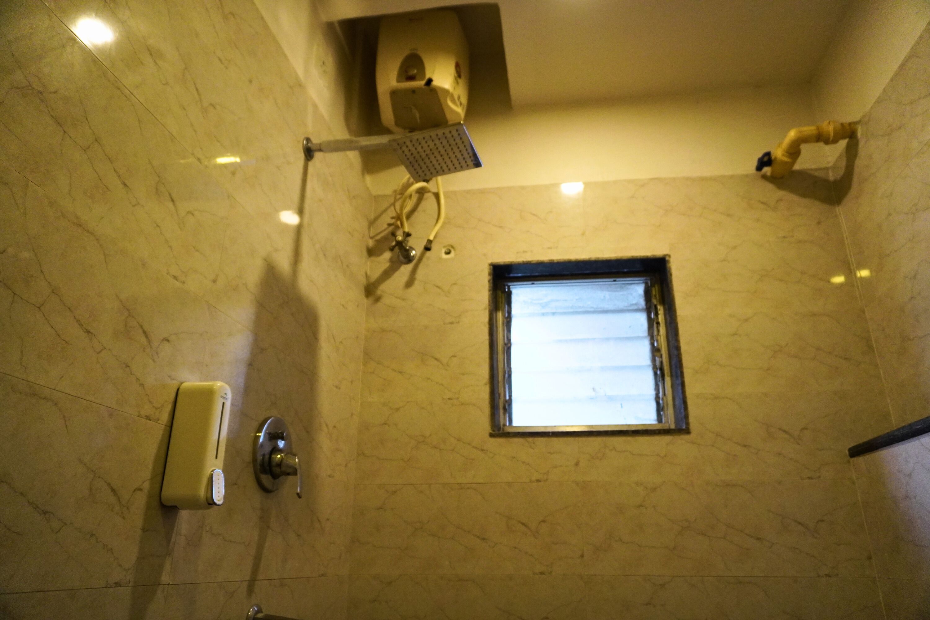 A bathroom with a marble floor, a window, a handheld showerhead, and a soap dispenser.
