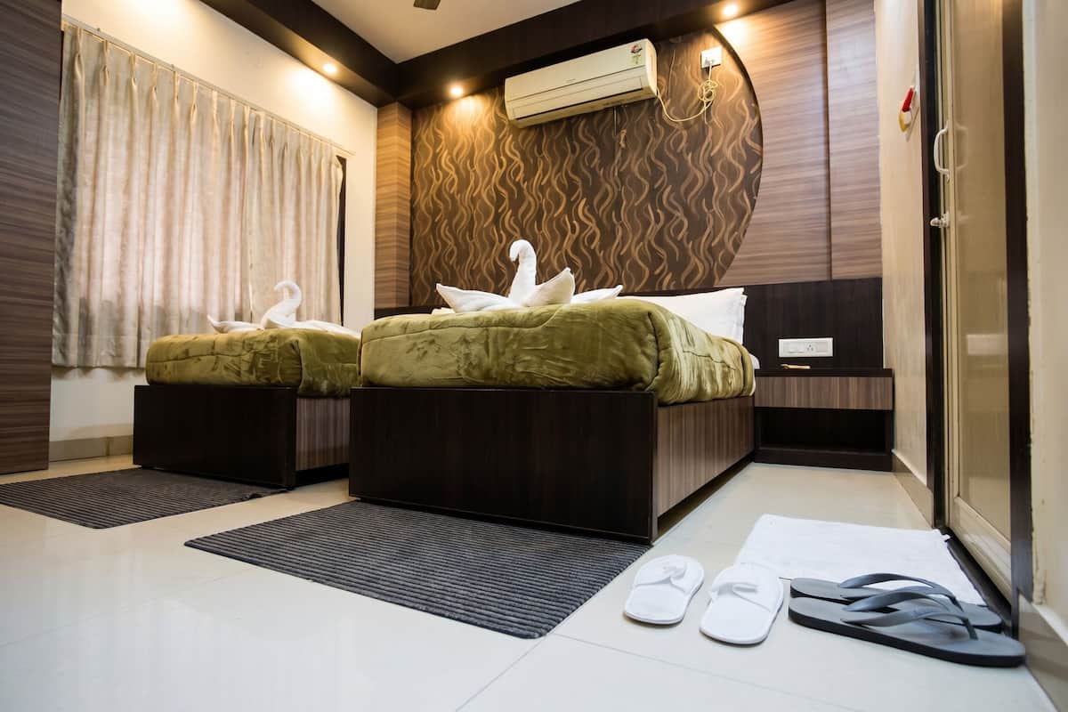 Habitación de hotel con dos camas, un ventanal con cortinas, aire acondicionado y pantuflas en el suelo.
